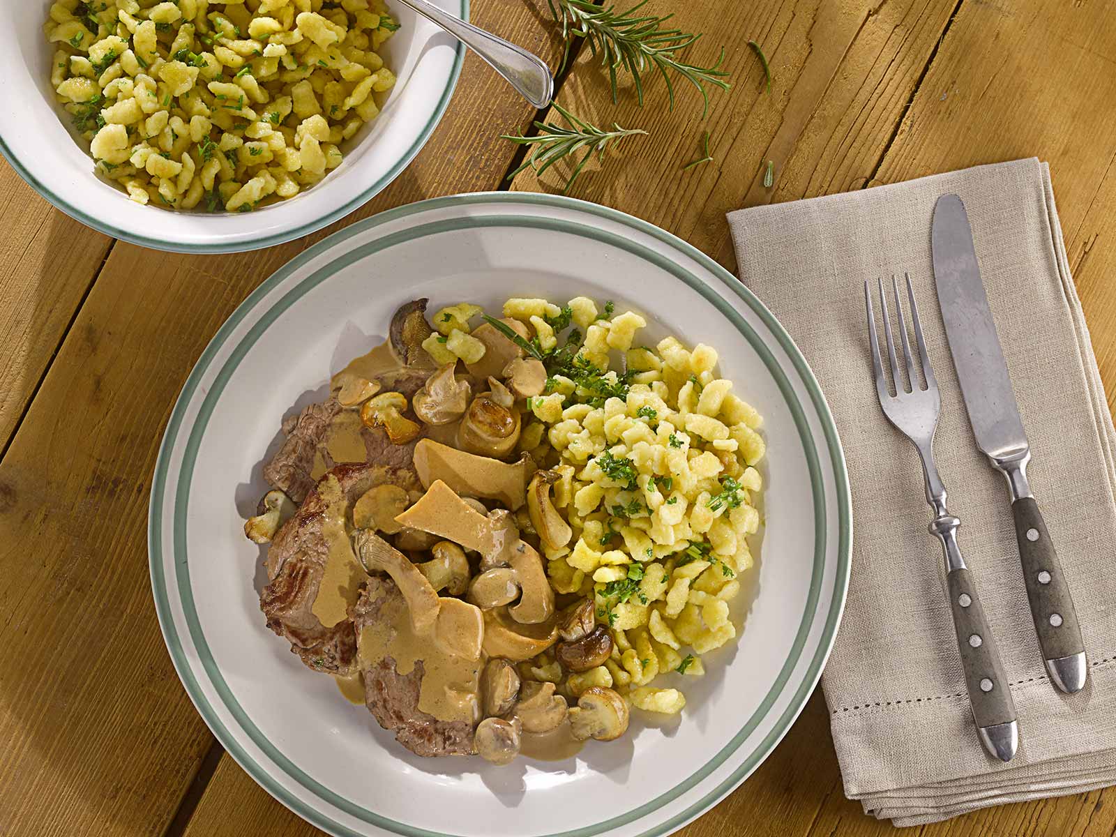Tress Rezept für Rehschnitzel mit Pilzrahmsoße und Kräuter-Knöpfle, angerichtet auf einem weißen Teller mit grünem Rand.