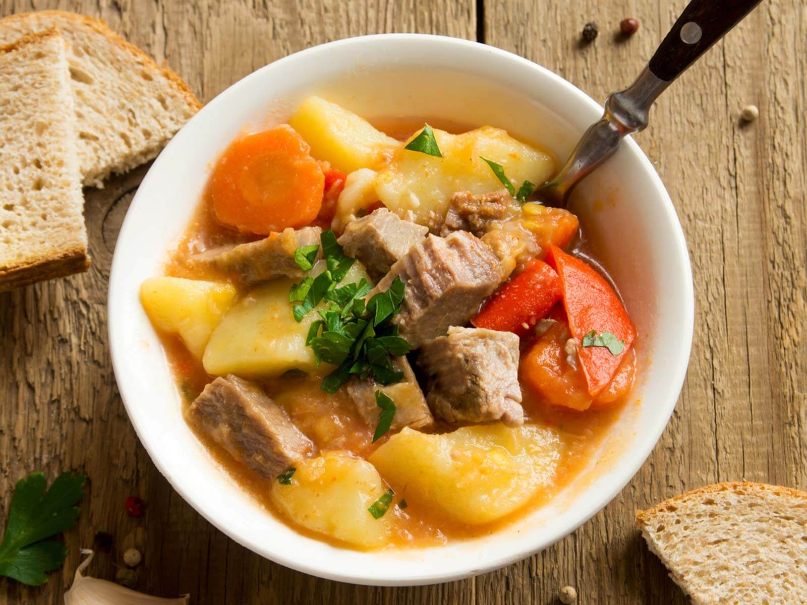Eine Suppenschale mit Fleischstücken, Kartoffeln und Karotten, dazu Brotscheiben