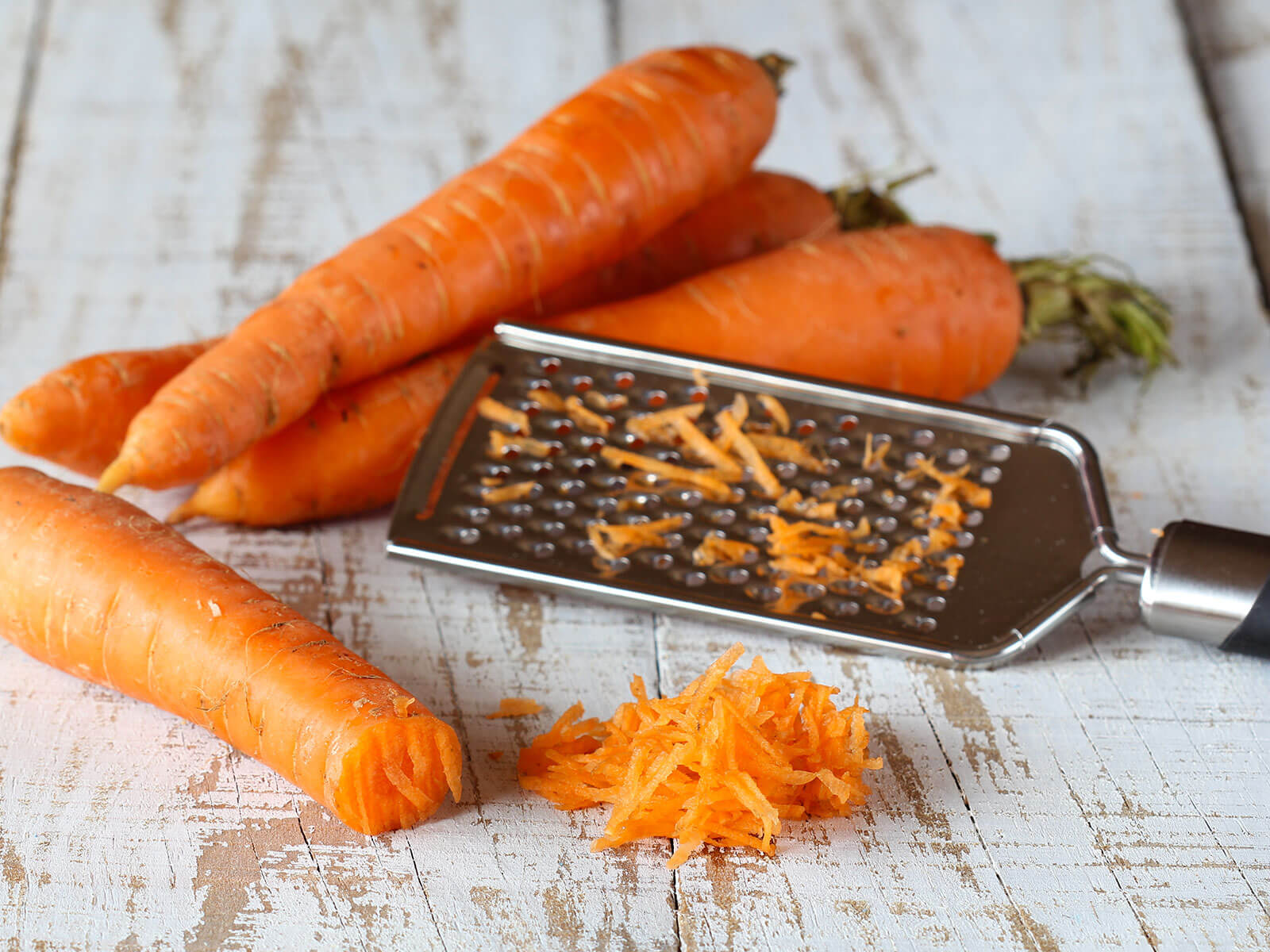 Vier rohe Karotten liegen bereit um einer Handreibe für ein Tress-Rezept klein geraspelt zu werden